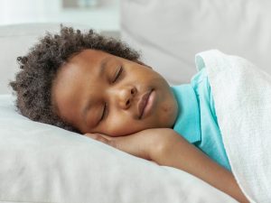 Close-up of a boy's head and shoulders resting on a pillow, with his eyes closed and his hand nestled under his face.