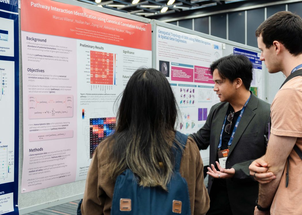 Marcus Villena points to a large poster displaying his research. Two people standing next to him look towards what he is pointing at.