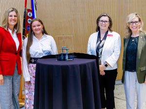 Four people stand behind a table that has an Inukshuk incased in plexiglass on it.