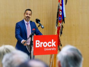 A man stands at a podium labelled ‘Brock University’ during an announcement.