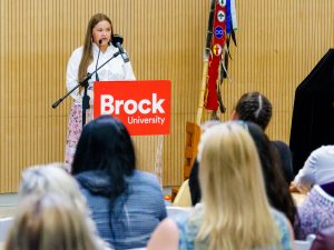 A woman speaks at a podium in front of a large crowd at Brock University.