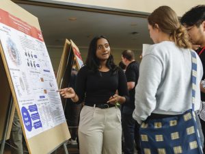 A university student points to a research poster as she speaks to people about it.