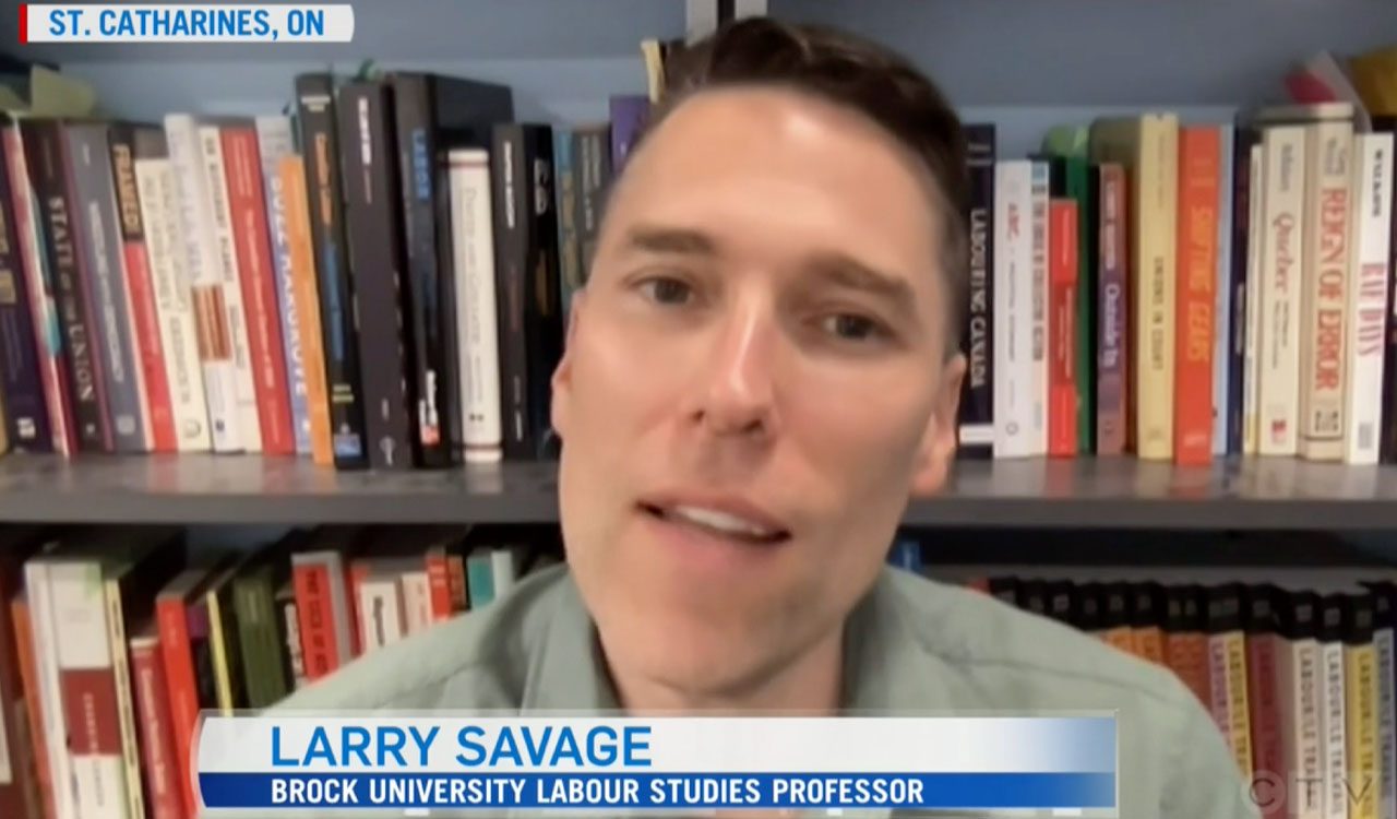 Professor Larry Savage pictured doing a television interview wearing a green collared shirt in front of a book shelf. His name and Brock University job title are shown at the bottom of the image.