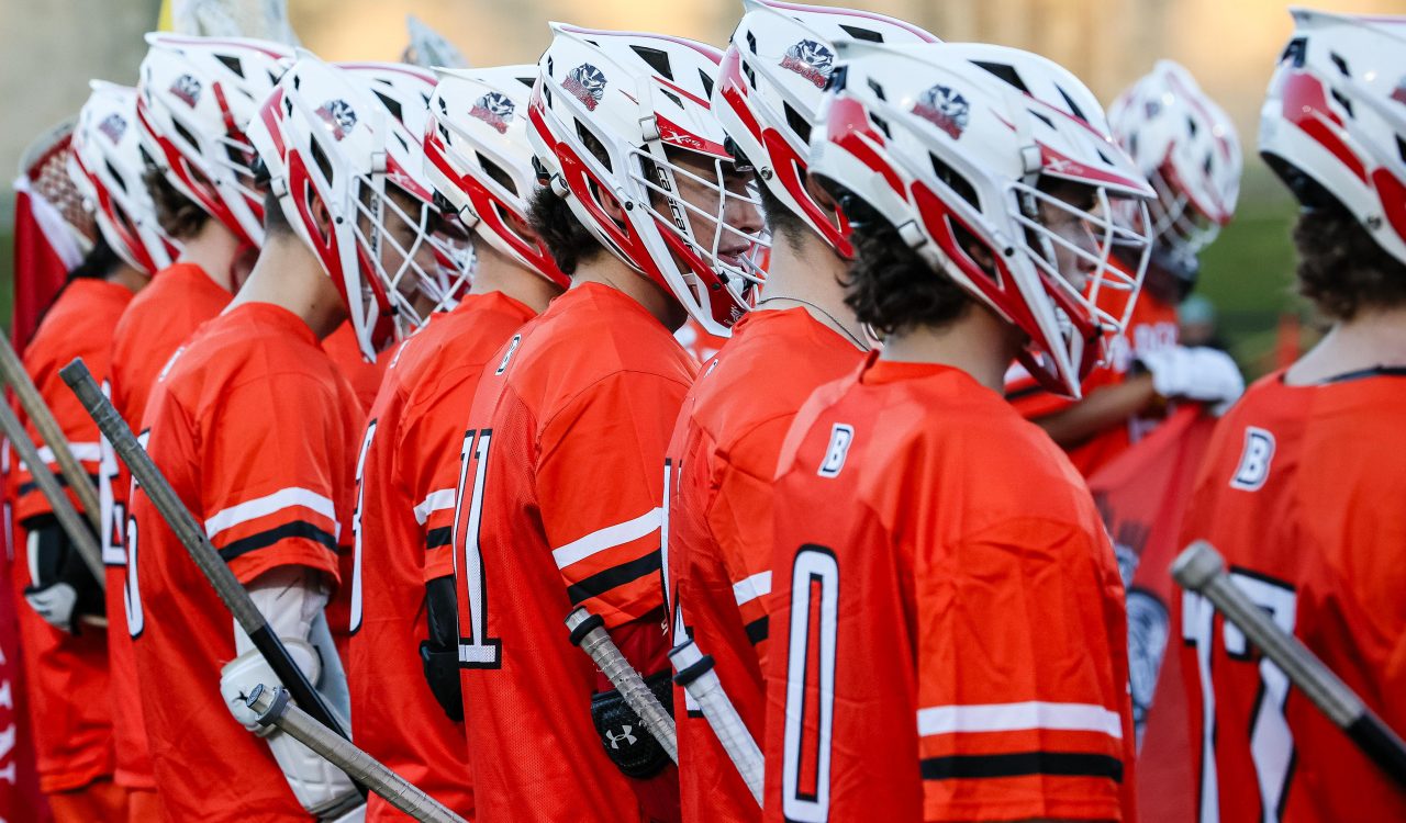 Men’s lacrosse players stand in a group wearing helmets and uniforms outdoors at Brock University.