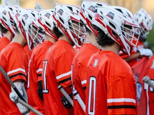 Men’s lacrosse players stand in a group wearing helmets and uniforms outdoors at Brock University.