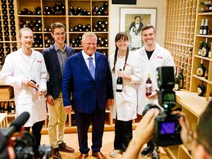 Five people pose for photos in a wine cellar. Three are wearing lab coats.