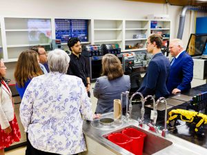 A group of people face a young man who is speaking in an engineering lab.