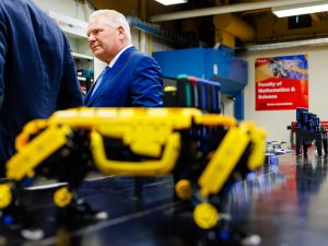 A man stands in an engineering lab with out-of-focus tools on a table in front of him.