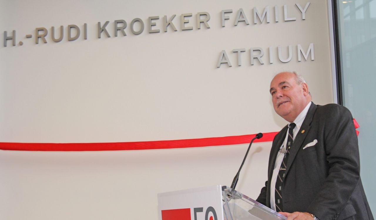 A man stands at a podium in front of a wall draped with a red ribbon.