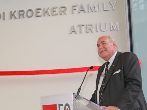 A man stands at a podium in front of a wall draped with a red ribbon.