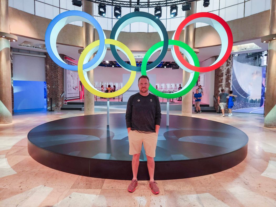 Colin Freeman poses in front of the Olympic rings inside an indoor hospitality venue.