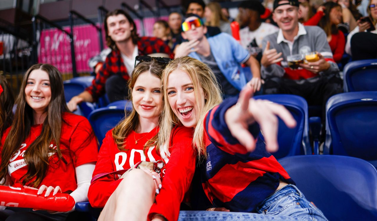 A group of women wearing Brock University sweaters and T-shirts cheer while sitting in arena seats at the Meridian Centre in downtown St. Catharines.