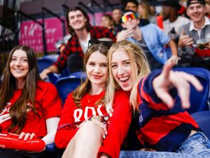 A group of women wearing Brock University sweaters and T-shirts cheer while sitting in arena seats at the Meridian Centre in downtown St. Catharines.