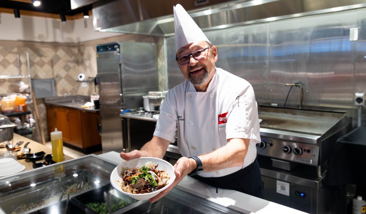 A chef holds up a bowl of stir fry in a kitchen.