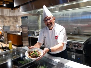 A chef holds up a bowl of stir fry in a kitchen.