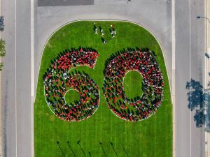 Hundreds of people wearing red shirts form a large 60 on the green lawn of a university. They are pictured from the sky.