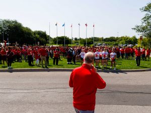 People in red shirts stand on a green field outside at Brock University.