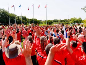 People raise their arms in celebration while standing outside together on a field.