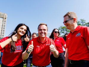 People in red shirts stand in front of Brock University's Schmon Tower.