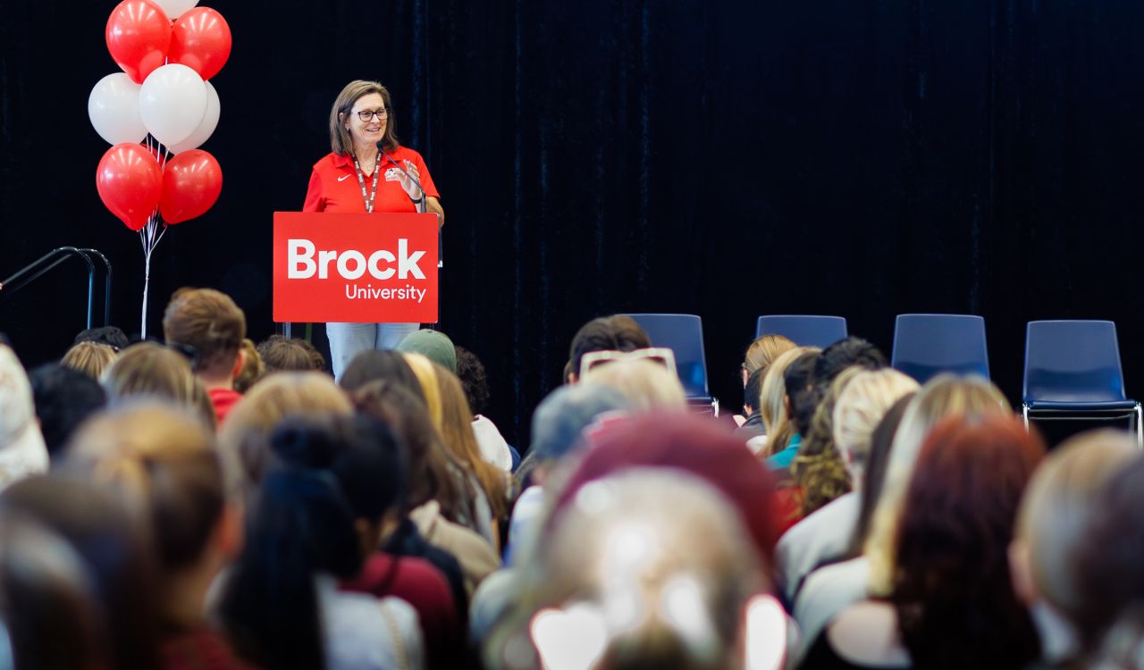 A woman stands at a podium in front of a large crowd.