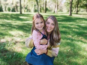 A young girl and her mother smile and hug for a photo in a park.