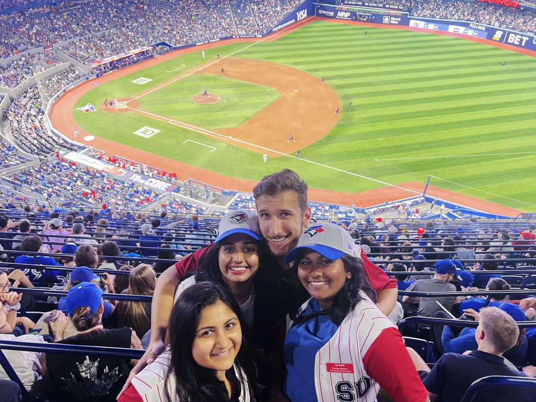 Four university students pose for a photo at a baseball game.