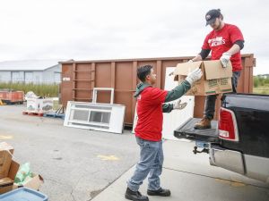 Two university students in red shirts load boxes onto the back of a truck in a parking lot during a volunteer event.