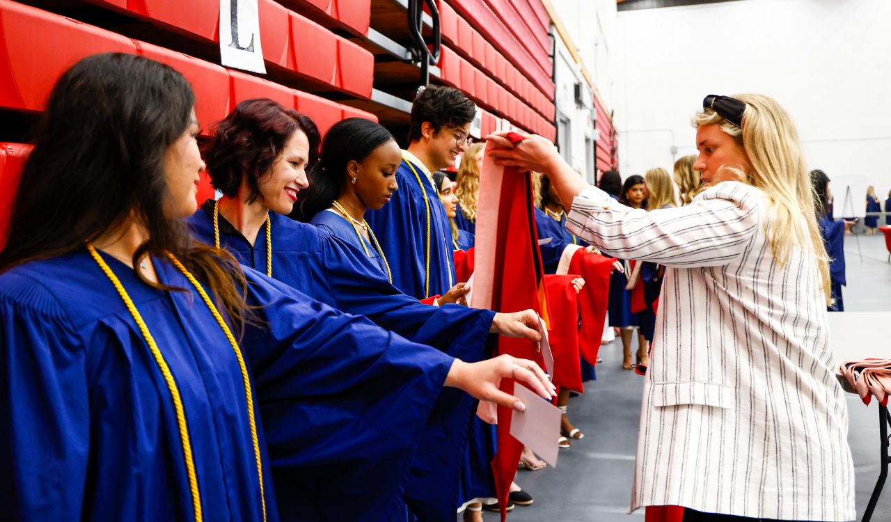 Women puts graduation hoods on Brock students wearing gowns while waiting in line to graduate.