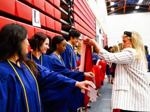 Women puts graduation hoods on Brock students wearing gowns while waiting in line to graduate.