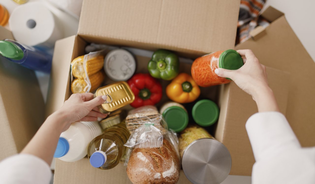 Close-up view of hands packing grocery items into a cardboard box.