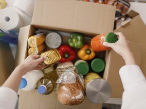 Close-up view of hands packing grocery items into a cardboard box.