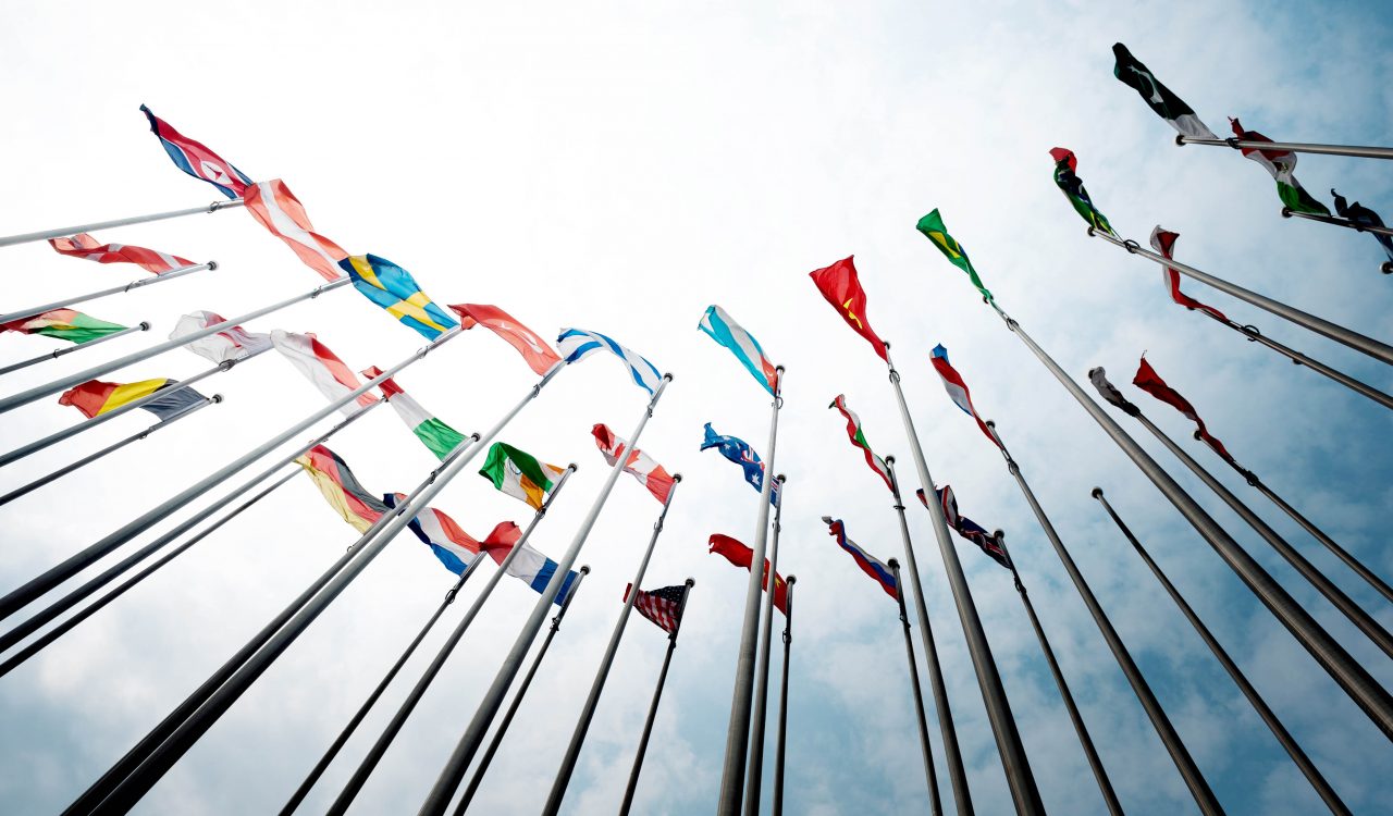 Rows of national flags wave against a blue sky.