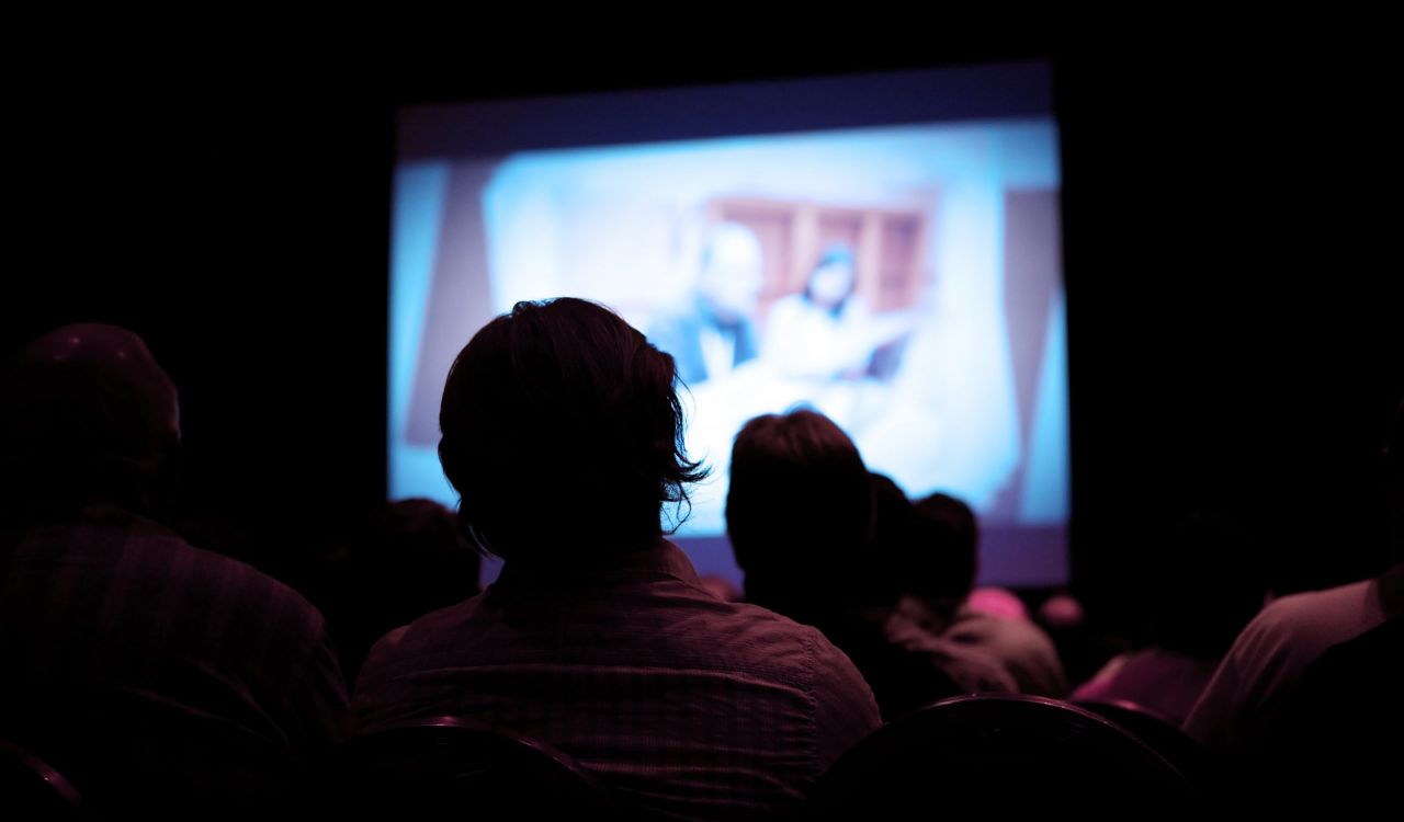 People in a dark theatre watch a movie screen.