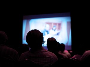 People in a dark theatre watch a movie screen.