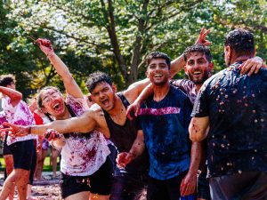 A group of four students, men and women, smile into the sun while covered in grapes.