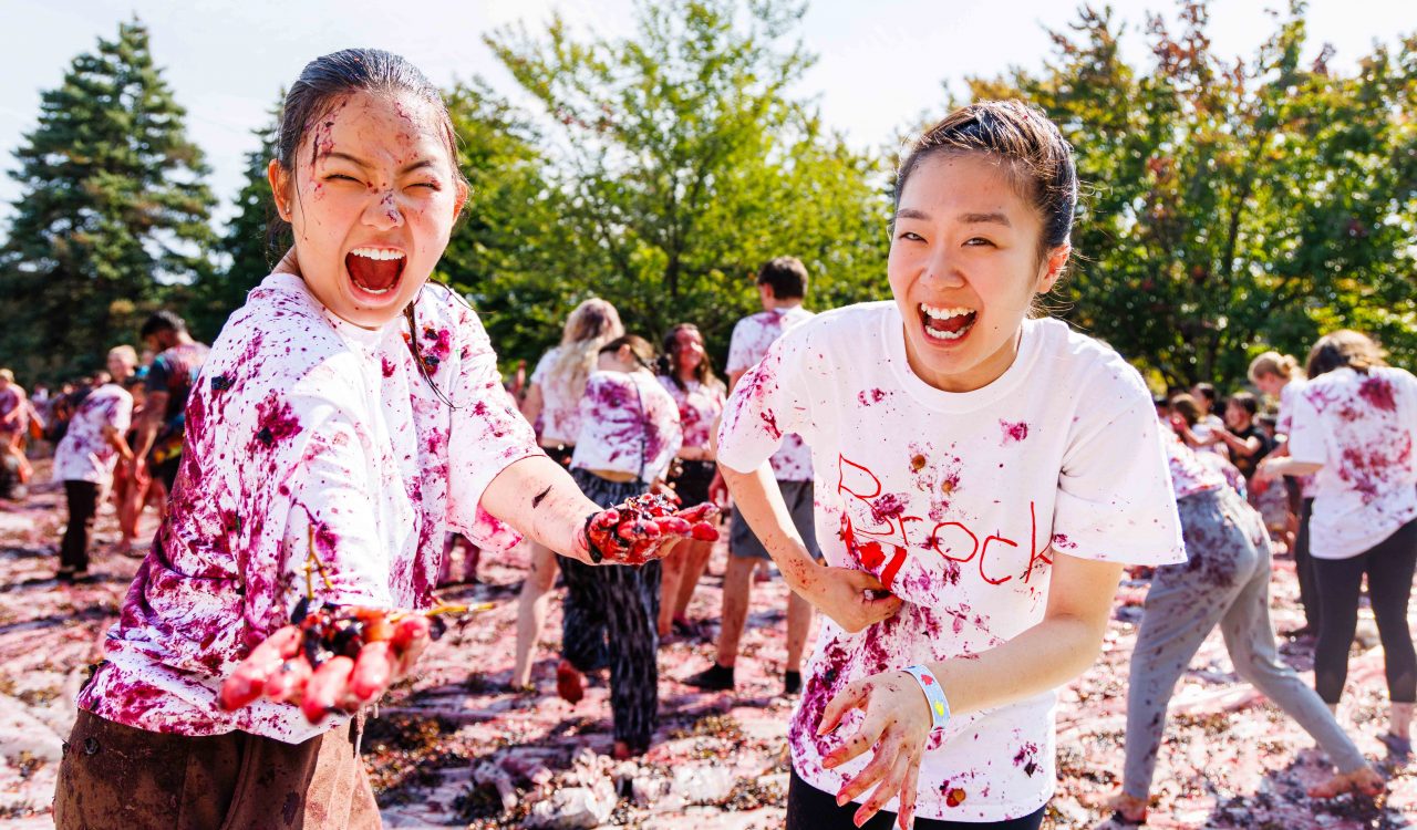 A pair of women laugh with excitement while being covered in grapes as they participate in Brock University’s grape stomp outdoors on main campus.