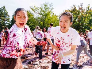 A pair of women laugh with excitement while being covered in grapes as they participate in Brock University’s grape stomp outdoors on main campus.