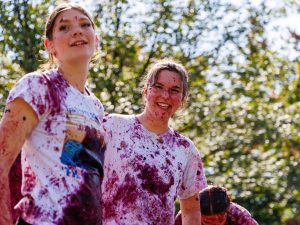 Two women wearing white shirts while covered in grapes smile outdoors at Brock University.