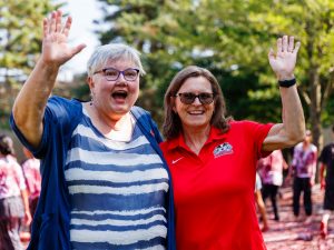 Two women smile and wave during Brock University’s Grape Stomp outdoors.