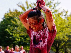 A man squeezes a handful of grapes over his head outdoors at Brock University.