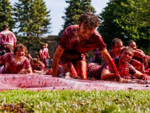 A group of male students crawl across a grape-covered tarp outdoors at Brock University.