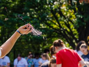 A close-up of a student’s hand throwing crushed grapes outdoors on Brock University’s main campus amongst trees outdoors.