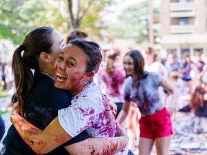 A woman laughs while hugging another woman in front of a sea of people outdoors at Brock University’s main campus.