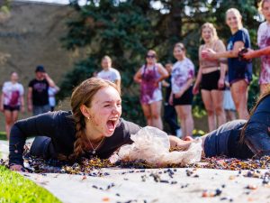 A woman yells while sliding through grapes as her fellow students cheer her on outside at Brock University.