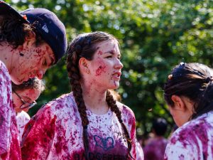 A woman looks off into the distances while surrounded by friends who are all covered in grapes.