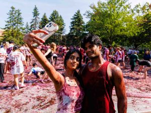 A woman holds up her phone to take a selfie with a man with Brock University’s annual tradition, Grape Stomp, happening in the background.