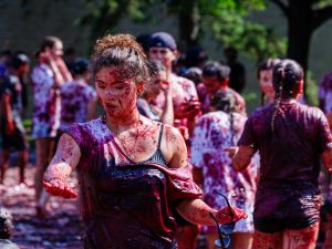 A woman holds up her phone to take a selfie with a man with Brock University’s annual tradition, Grape Stomp, happening in the background.