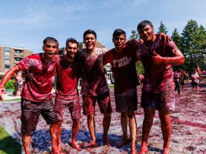 A group of five men smile and give thumbs up as they stand covered in red grapes outside at Brock University.