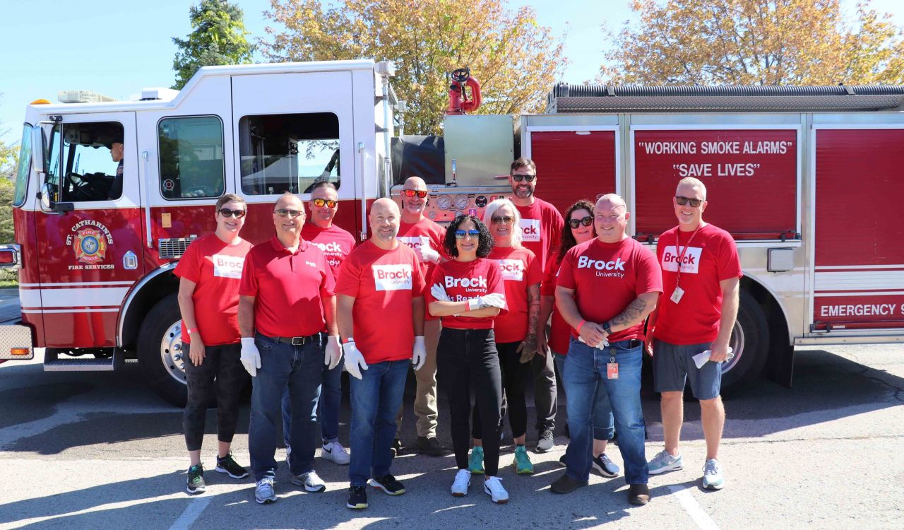 A large group of people in red shirts pose for a photo in front of a fire truck.