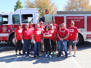 A large group of people in red shirts pose for a photo in front of a fire truck.